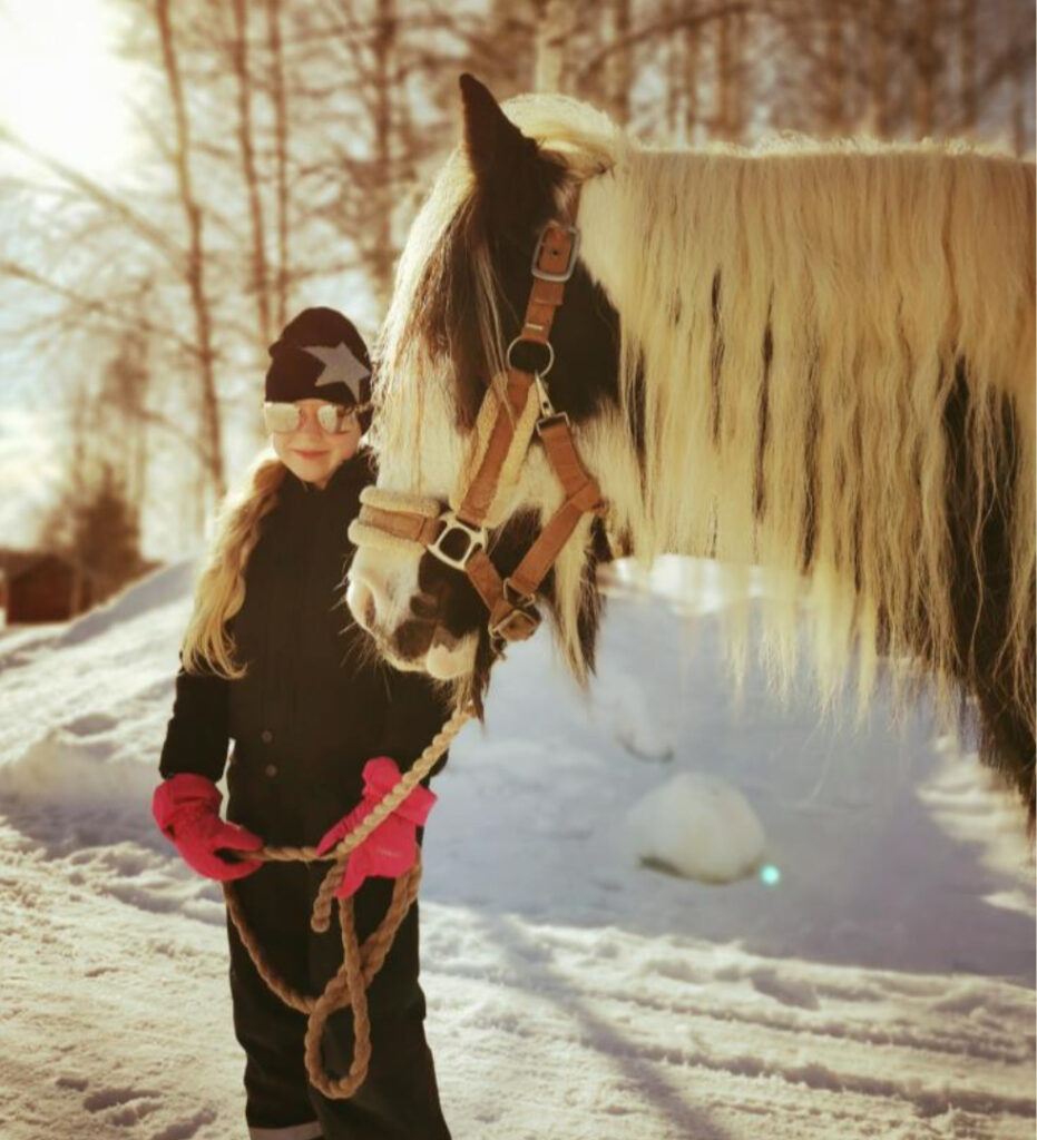 Tyttö ja hevonen talvella auringonpaisteessa ulkoilemassa